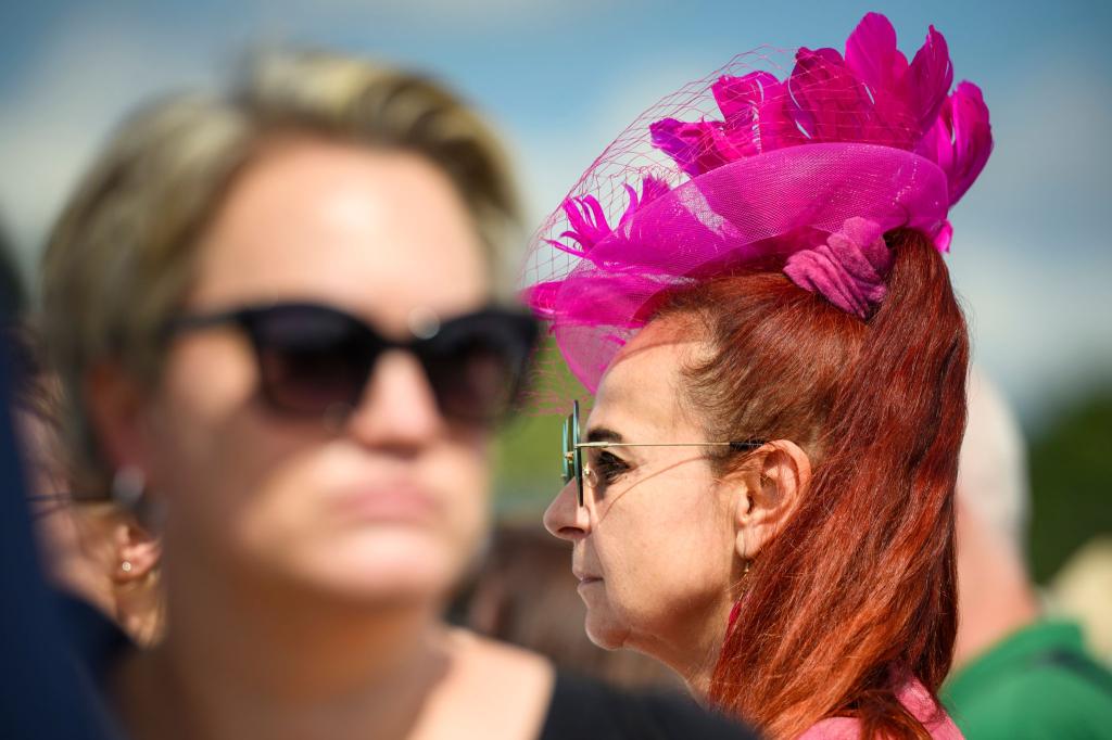 Mit einem pinkfarbenem Hut geht eine Frau über die Galopprennbahn Hamburg Horn beim Idee Derby-Meeting 2024 - Foto: Gregor Fischer/dpa