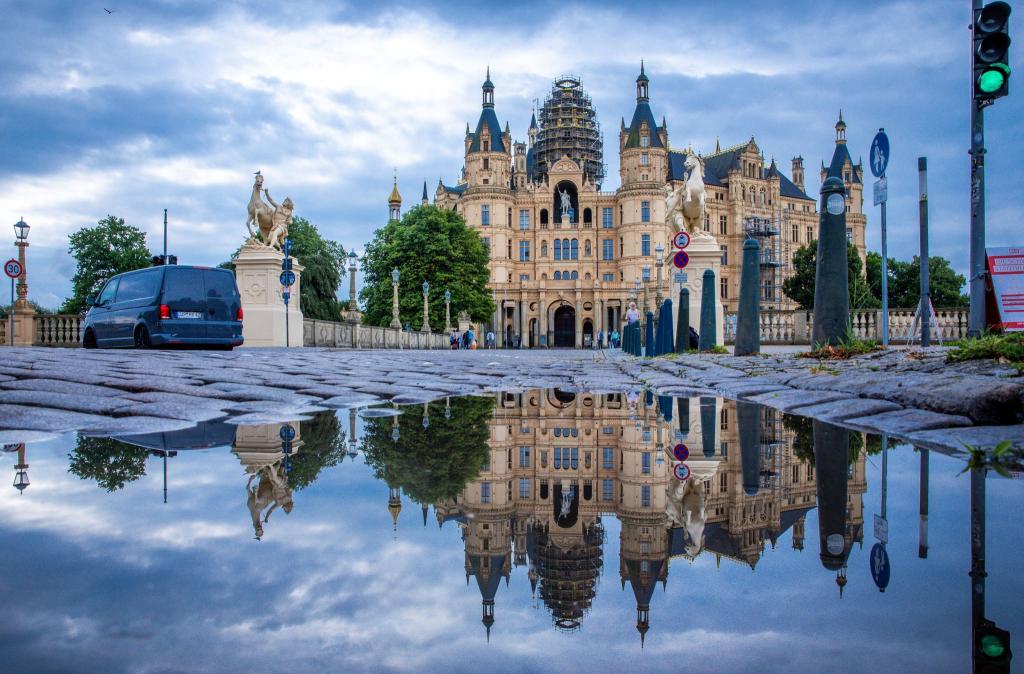Das Schweriner Schloss spiegelt sich in einer Pfütze. Am 27.07.2027 soll in Neu-Dehli (Indien) über die Aufnahme des Residenzensembles Schwerin auf die begehrte Unesco-Welterbeliste entschieden werden - Foto: Jens Büttner/dpa