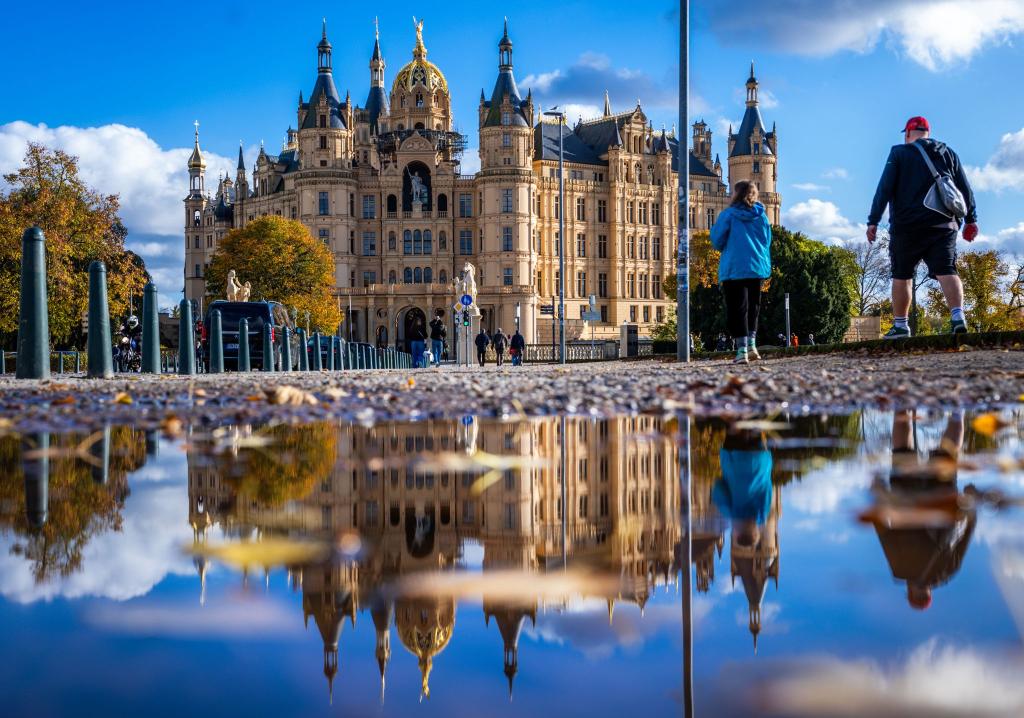 Milder Herbst: Schweriner Schloss spiegelt sich in einer Pfütze. - Foto: Jens Büttner/dpa