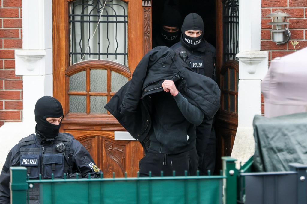 Polizeibeamte führen einen Tatverdächtigen aus einem durchsuchten Haus. - Foto: Christoph Reichwein/dpa